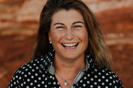 Catherine Marriott, head and shoulders, wearing blue shirt with white spots, against an out of focus reddish-brown patterned background