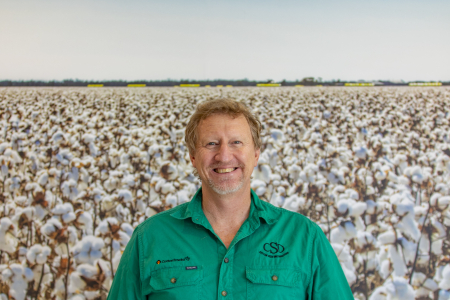 Mick Bange, head and shoulders, wearing green shirt with CSD logo on left side of chest, with field of cotton in background