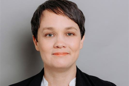 Rachael Chay, head and shoulders, in black jacket with white shirt, against a grey background