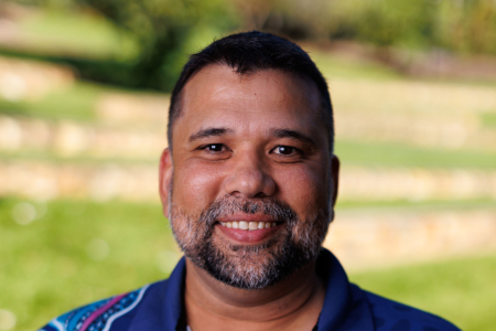 Troy Garling, head and shoulders, wearing blue shirt with "get up, stand up, show up" logo on left side of chest and swirling coloured pattern on right shoulder and chest