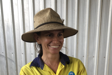 Dr Tansyn Noble, head and shoulders, wearing wide brimmed hat and yellow hi-vis shirt with CSIRO logo, corrugated metal wall in background