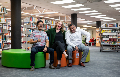 three students sitting on chairs inside the CDU Alice Springs campus library