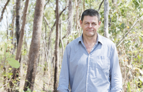 Lindsay Hutley, head to waist, wearing a blue shirt, with trees and shrubs in the background