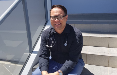 Man sitting on stairs smiling with stethoscope around his neck.