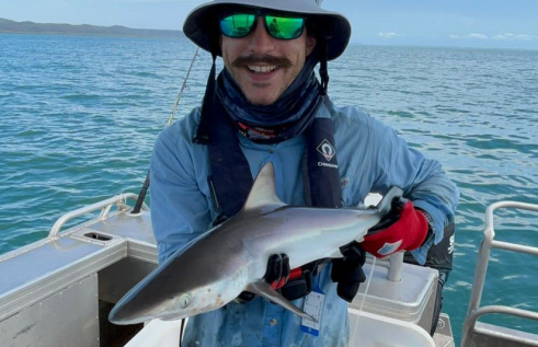 Person wearing hat and sunglasses standing in a boat holding a small shark