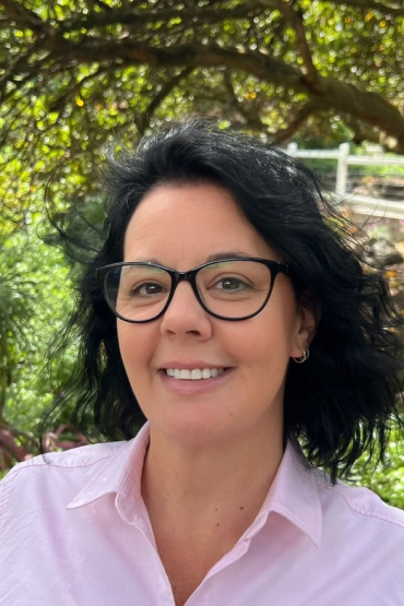 female with a pink smart shirt and black glasses standing outdoors 